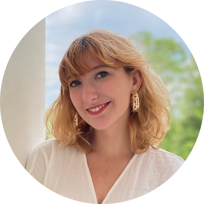 a photo of a white woman with orangeish blonde hair smiling in a white shirt with red lipstick and large gold hoop earrings
